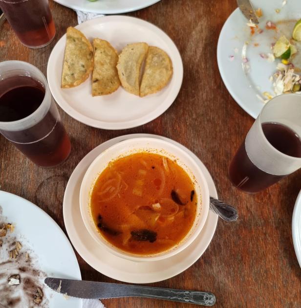 Eine Schüssel Suppe, Tacos und Getränke stehen auf einem Holztisch.