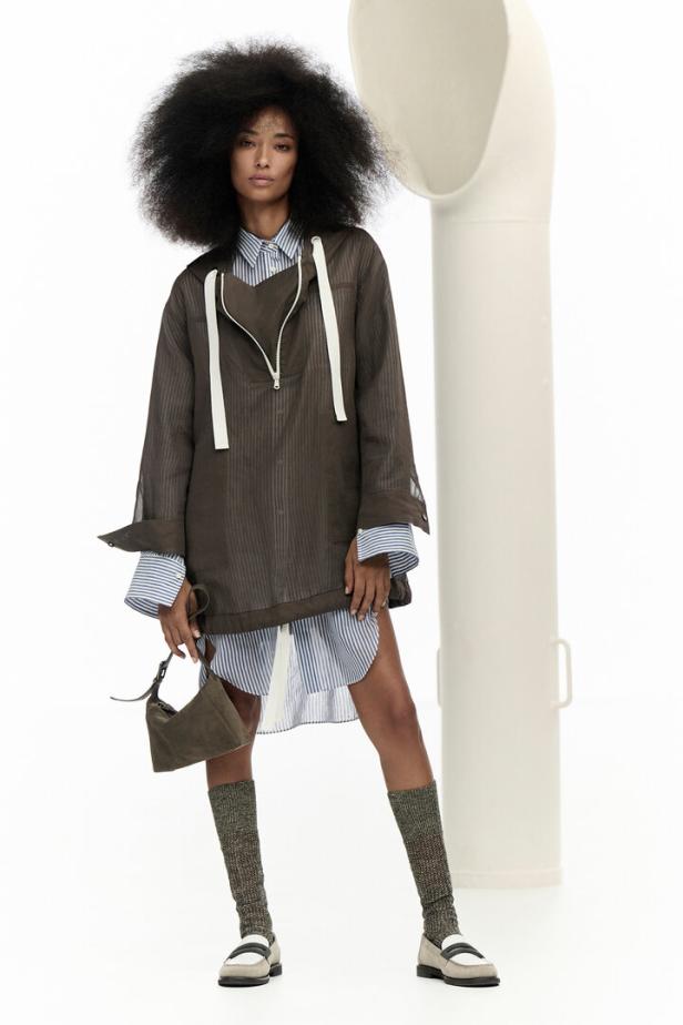 Eine Frau mit Afro trägt ein braunes Outfit mit gestreiftem Hemd, Kniestrümpfen und Loafern.