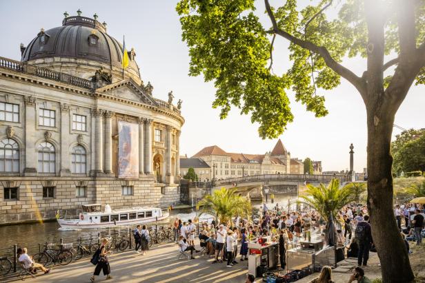 Die Museumsinsel in Berlin: Menschen laufen am Kanal entlang, ein Boot fährt über den Kanal.