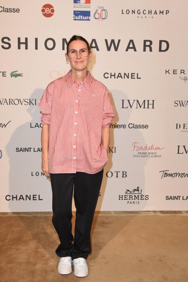 Eine Frau mit Brille posiert vor einer Wand mit Logos für den Fashion Award.
