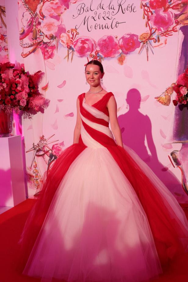 Eine Frau in einem rot-weißen Ballkleid vor einem Hintergrund des „Bal de la Rose 2022 Monaco“.
