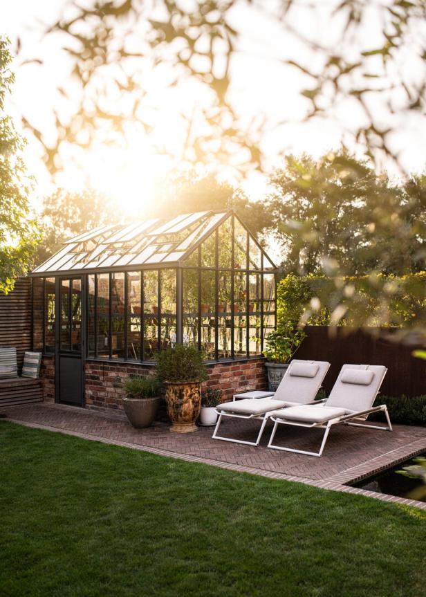 Ein Gewächshaus und zwei Liegestühle in einem gepflegten Garten im Abendlicht.