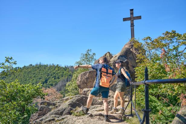 Ein Paar wandert im Harz an einem Gipfelkreuz vorbei.