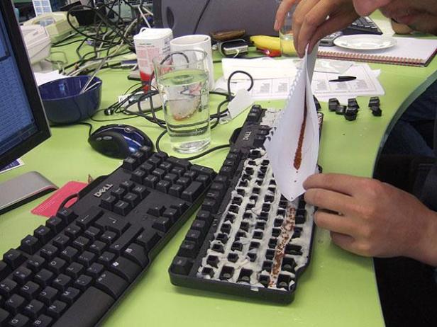 Eine Person reinigt eine Computertastatur mit einem Papier und einer braunen Substanz.