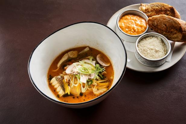 Eine Schüssel Fischsuppe mit Brot, Sauce und geriebenem Käse auf einem Teller.
