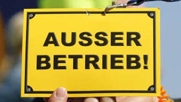 Ein gelbes Schild mit der Aufschrift „AUSSER BETRIEB!“ wird von einer Hand gehalten.