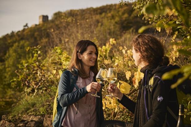 Zwei Frauen heben ihre Riesling-Gläser und feiern den Weingenuss inmitten der Weinreben.