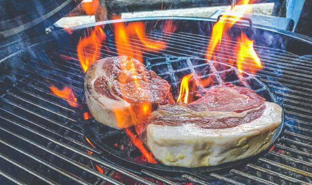 Zwei Steaks brutzeln auf einem Grill mit offenen Flammen.