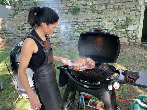Eine Frau grillt ein großes Tomahawk-Steak auf einem Grill im Freien.