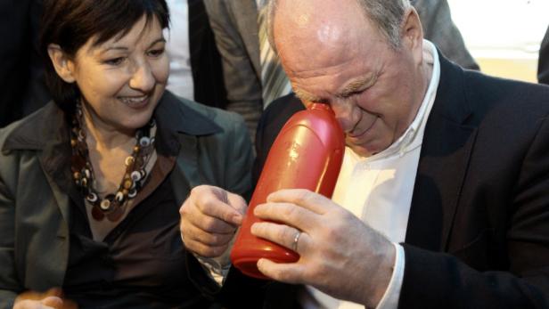 Ein Mann riecht an einer roten Plastikflasche, während eine Frau danebensteht und lächelt.