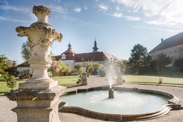 Ein Brunnen sprudelt im Garten eines Schlosses.