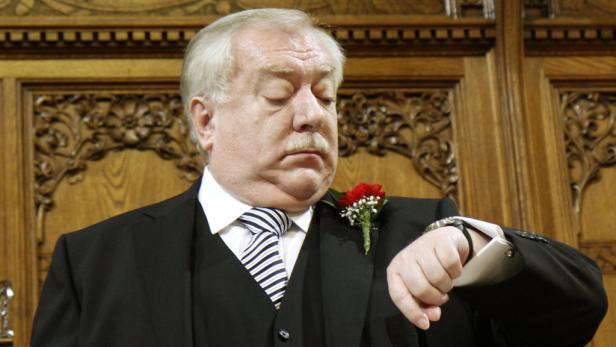 Ein Mann im Anzug blickt auf seine Armbanduhr.