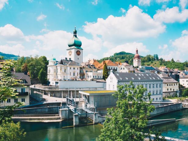 Blick auf eine Stadt mit einem Fluss und historischen Gebäuden unter blauem Himmel.