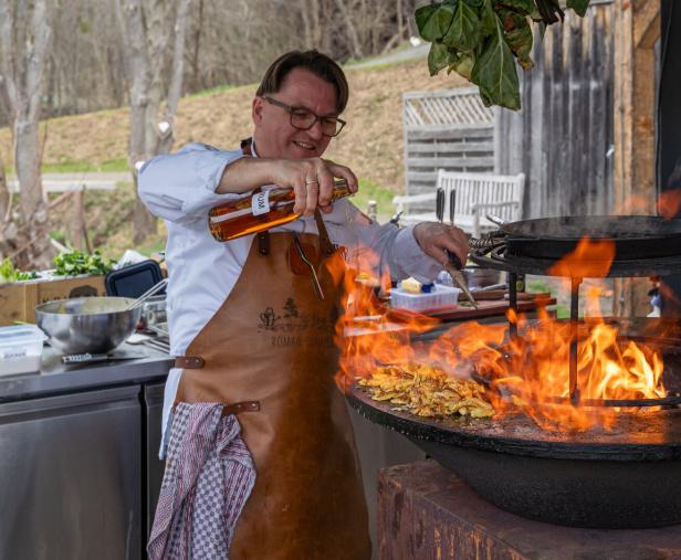 Ein Koch leert Rum über die Grillplatte, wo der Kaiserschmarrn draufliegt. Sie fängt Feuer, der Schmarrn karamellisiert.