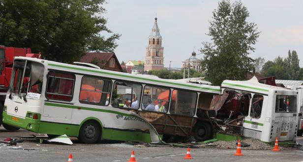 Zwei zusammengestoßene Busse stehen auf einer Straße, im Hintergrund eine Kirche.