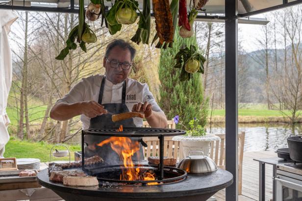 Der Koch legt ein dickes Steak auf den Grill über dem Feuer.