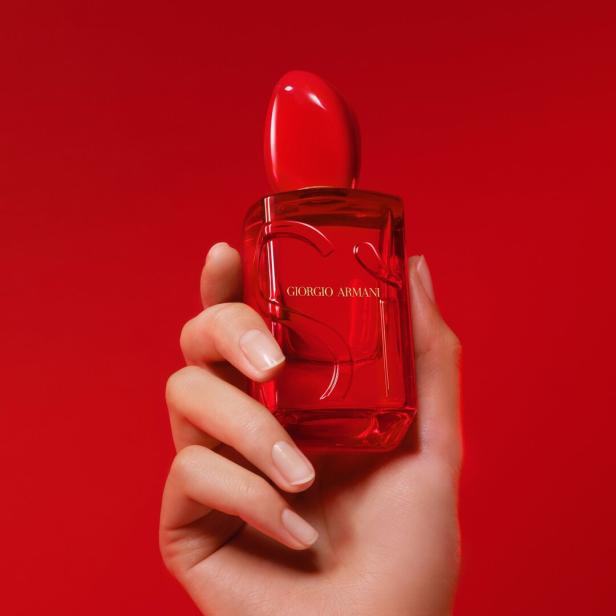 Eine Hand hält einen roten Flakon des Parfüms „Giorgio Armani Si Passione“ vor einem roten Hintergrund.