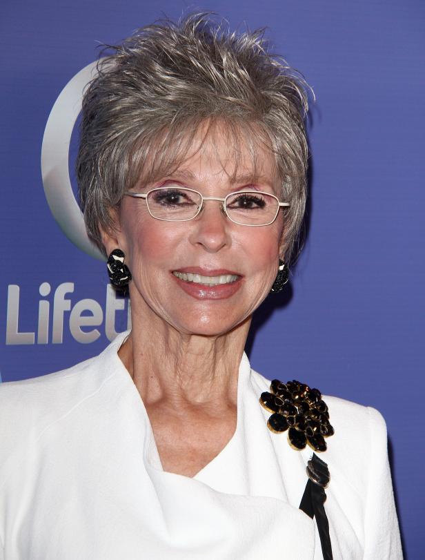 Rita Moreno lächelt auf einem Porträt vor einem blauen Hintergrund.