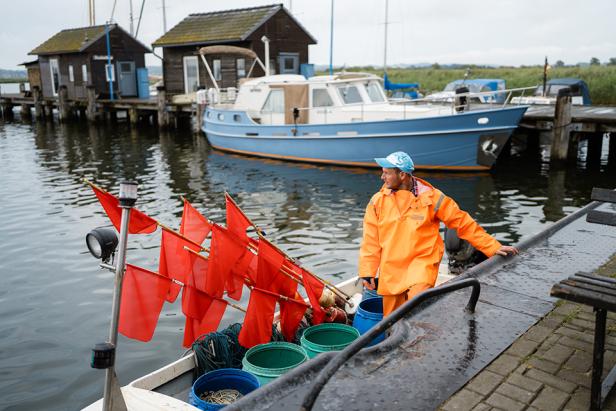 Ein Fischer in grell-orangenen, wasserabweisenden Klamotten steht auf einem Fischerboot.