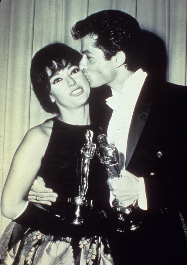Ein Mann küsst eine Frau, die zwei Oscar-Statuetten hält.