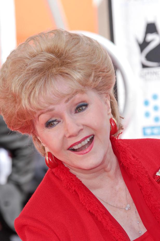 Debbie Reynolds lächelt in einem roten Blazer mit passenden Ohrringen.