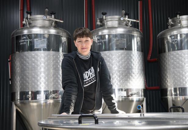 Eine Frau steht vor großen Edelstahltanks in einer Brauerei.