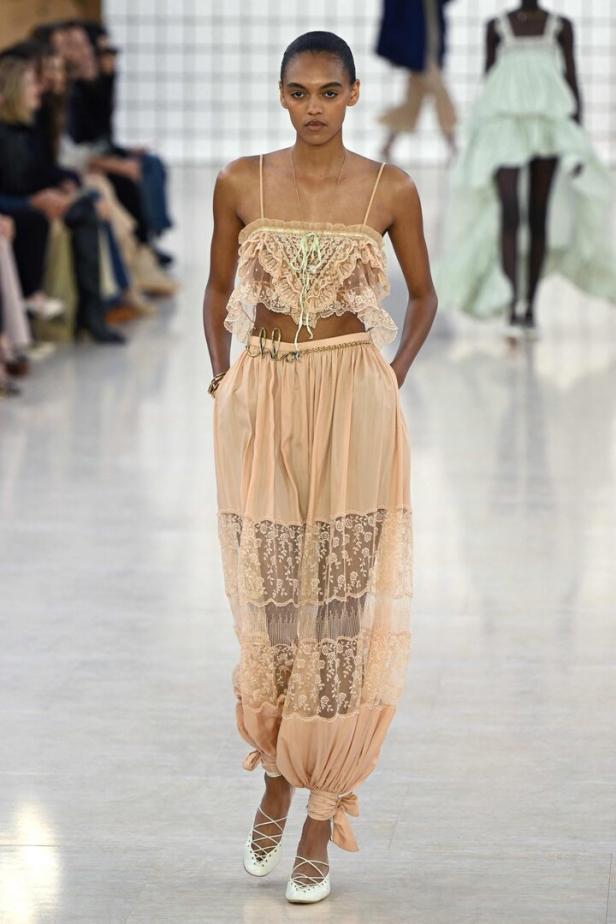 Ein Model präsentiert ein lachsfarbenes Kleid mit Spitze und einem „Chloé“-Gürtel auf dem Laufsteg.