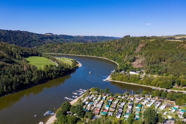 Vogelperspektive auf einen Fluss und eine Stadt, die harmonisch in die natürliche Umgebung eingebettet sind.