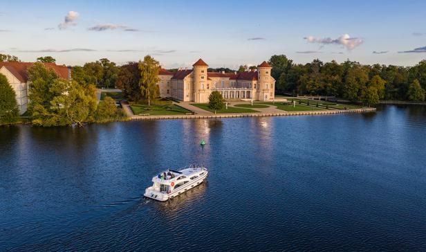 Ein Hausboot auf einem See vor einem Schloss.