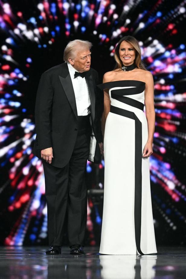 Donald und Melania Trump stehen auf einer Bühne vor einem farbenfrohen Hintergrund.