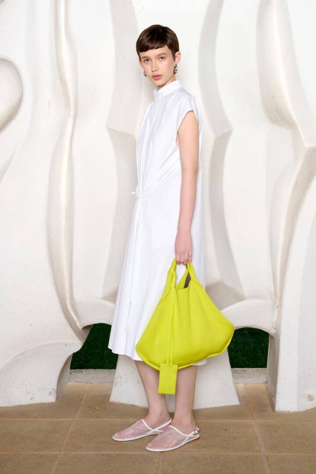 Eine Frau in einem weißen Kleid hält eine leuchtend gelbe Tasche.