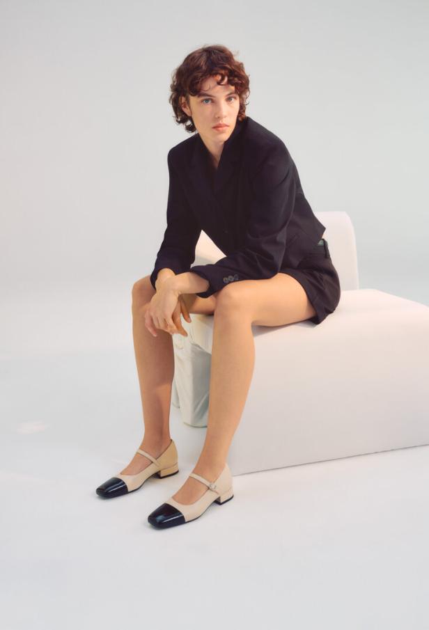 Eine Frau sitzt auf einem weißen Sessel und trägt Bicolor-Pumps von Vagabond.