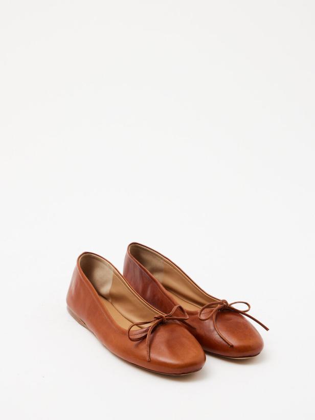 Ein Paar braune Ballerinas aus Leder mit Schleifen auf weißem Hintergrund.