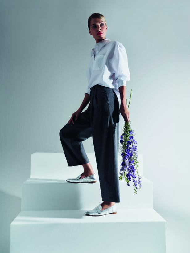 Eine Frau in weißem Hemd und grauer Hose steigt mit einem Blumenstrauß eine weiße Treppe hinauf.