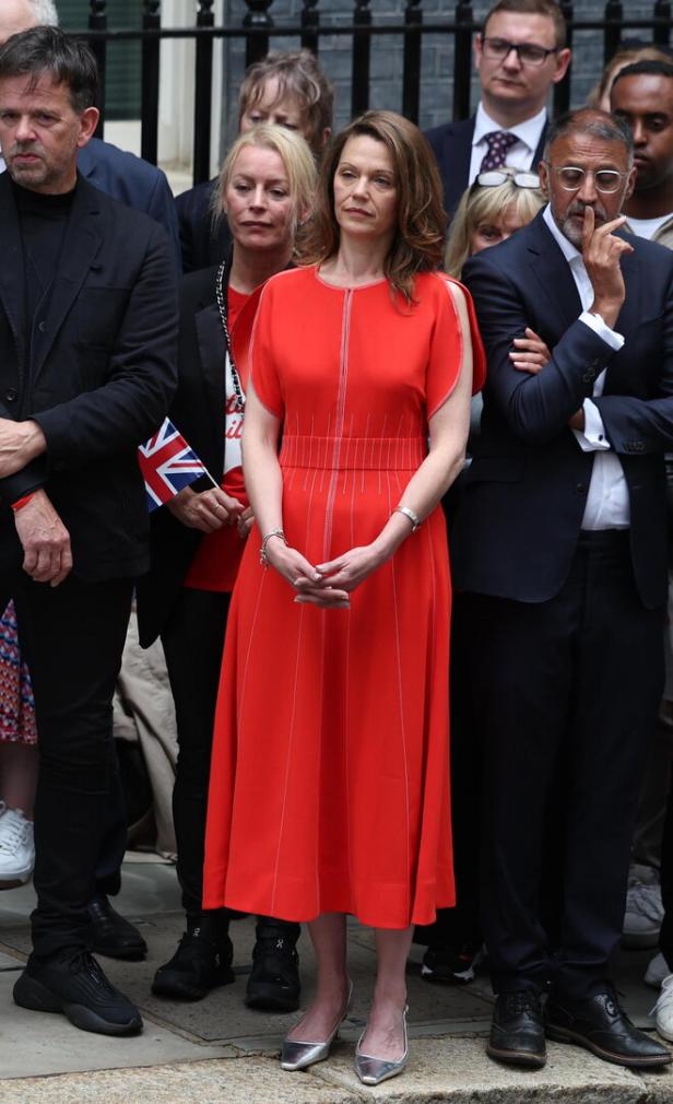 Eine Frau in einem roten Kleid steht vor einer Menschenmenge.