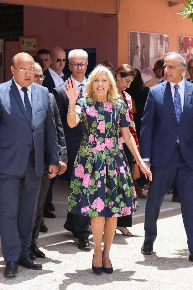 Jill Biden trägt ein geblümtes Kleid und winkt einer Menschenmenge zu.