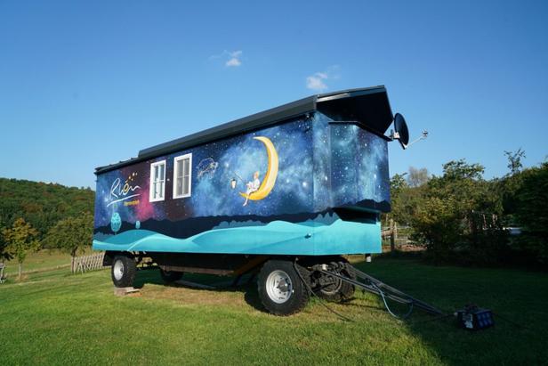 Ein kleines Haus auf Rädern mit einem Mond, der auf die Wand gemalt ist, steht vor einem klaren Himmel.