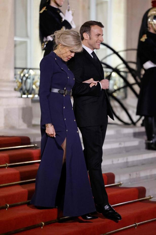 Emmanuel Macron und Brigitte Macron schreiten eine Treppe mit rotem Teppich hinunter.