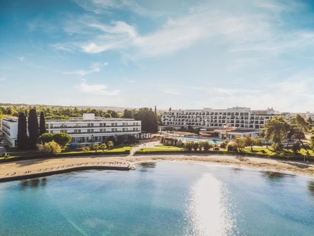 Eine Hotelanlage am Strand gelegen, davor ein türkisfarbenes Meer.