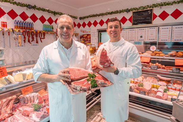 Zwei Metzger präsentieren stolz eine Auswahl an frischem Fleisch in ihrer Auslage.