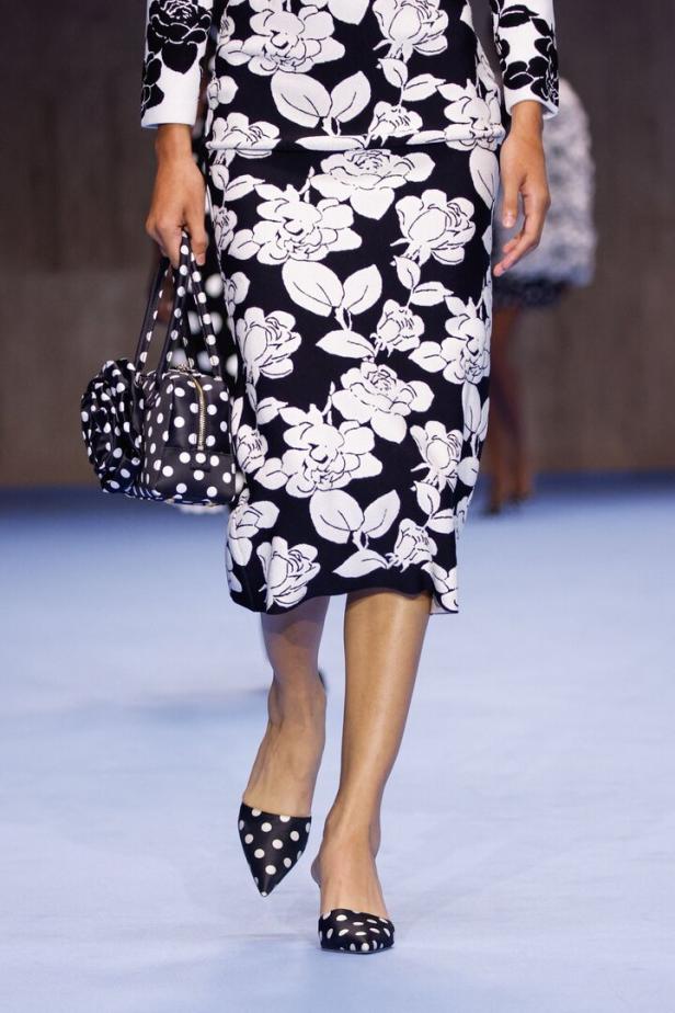 Eine Frau trägt ein schwarz-weißes Outfit mit Blumenmuster und eine gepunktete Handtasche und Schuhe.