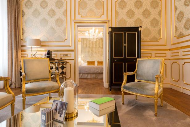 Ein luxuriöses Wohnzimmer mit goldenen Akzenten und Blick auf ein Schlafzimmer.