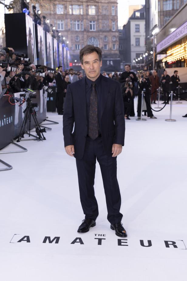 Ein Mann im Anzug posiert auf dem weißen Teppich für „The Amateur“.