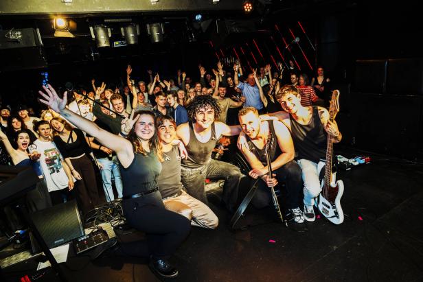 Eine Band posiert mit ihren Fans auf einer Bühne.