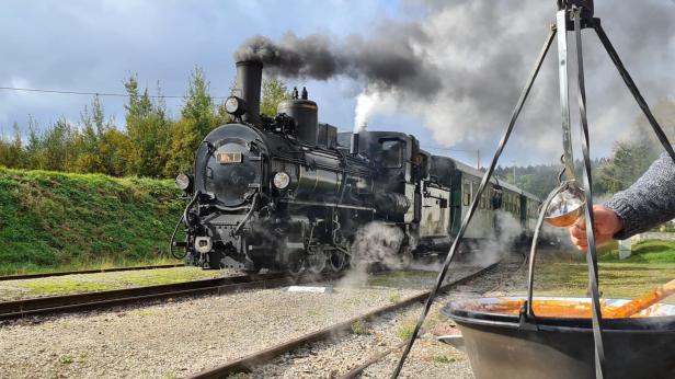 Ein Mann präsentiert einen Topf mit Speisen neben einem Gleis der Eisenbahn.