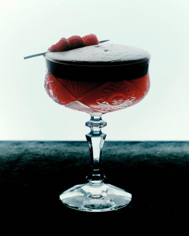Ein roter Cocktail in einem Kristallglas, garniert mit Himbeeren.