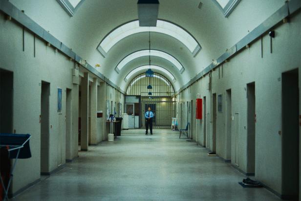 Ein Wachmann steht in einem langen, leeren Flur eines Gefängnisses.