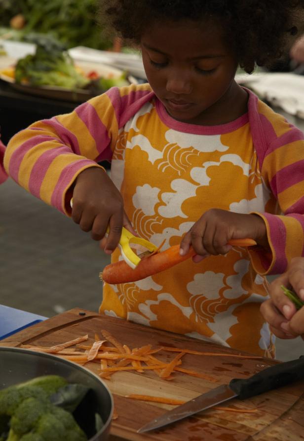 Ein junges Mädchen schält eine Karotte mit einem Sparschäler.