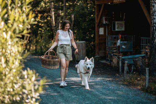 Eine Frau geht mit ihrem weißen Hund und einem Korb auf einem Kiesweg entlang.