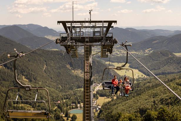 Eine Familie fährt mit einer Gondelbahn über eine bewaldete Berglandschaft.